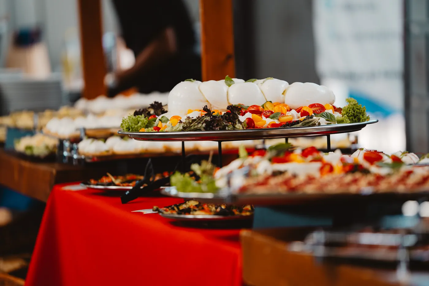 Présentoir à étages avec burrata, tomates et salade sur nappe rouge