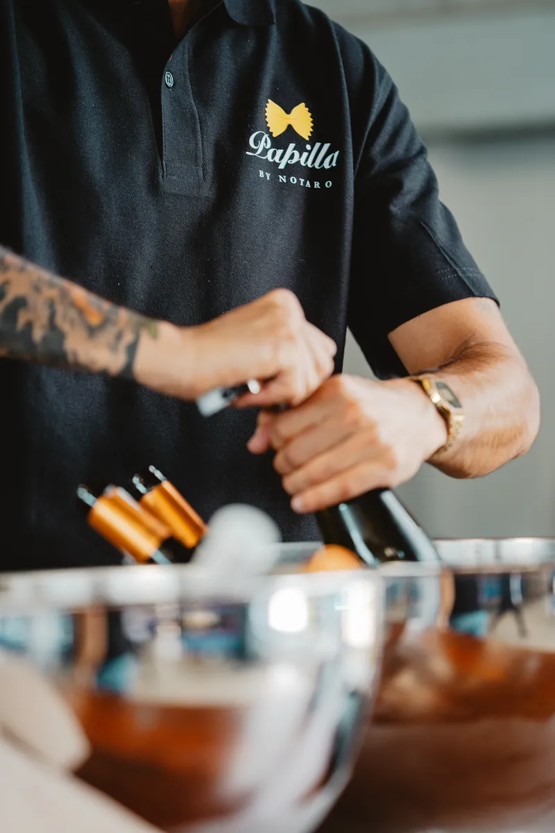 Un membre de l'équipe Papilla, polo brodé au logo, ouvre une bouteille de vin derrière le bar