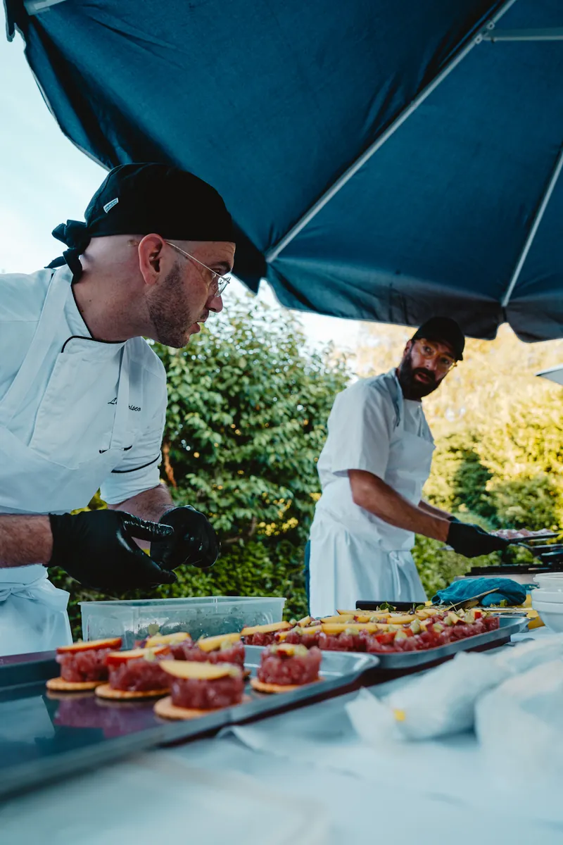 Deux chefs en veste blanche dressent des tartelettes sous une tente