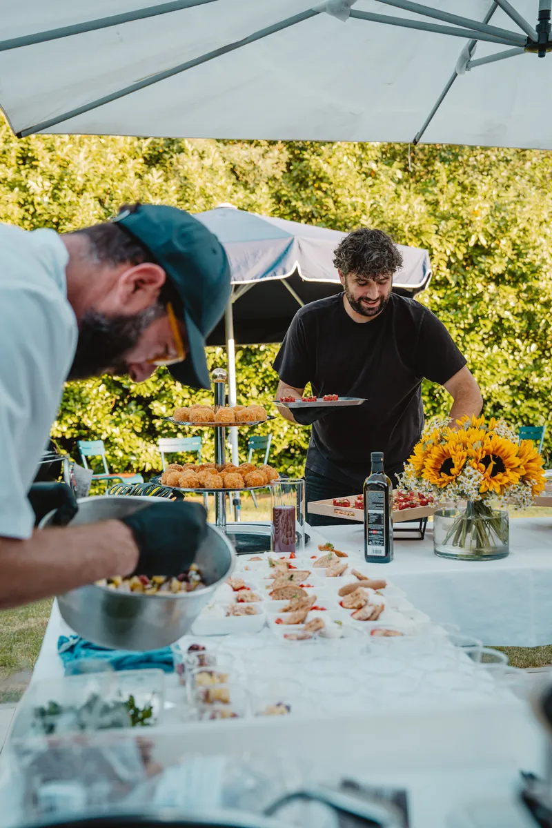 Deux chefs cuisinent sous une tente dans un jardin, tournesols au premier plan